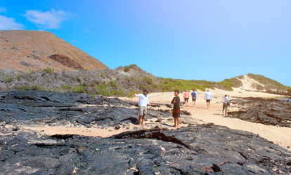 Personas caminando sobre lava negra en Bahía Sullivan en Galápagos.