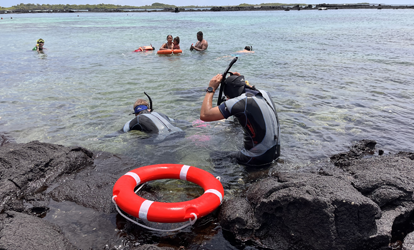 Grupo de personas preparándose para hacer snorkeling con una boya roja en el mar.